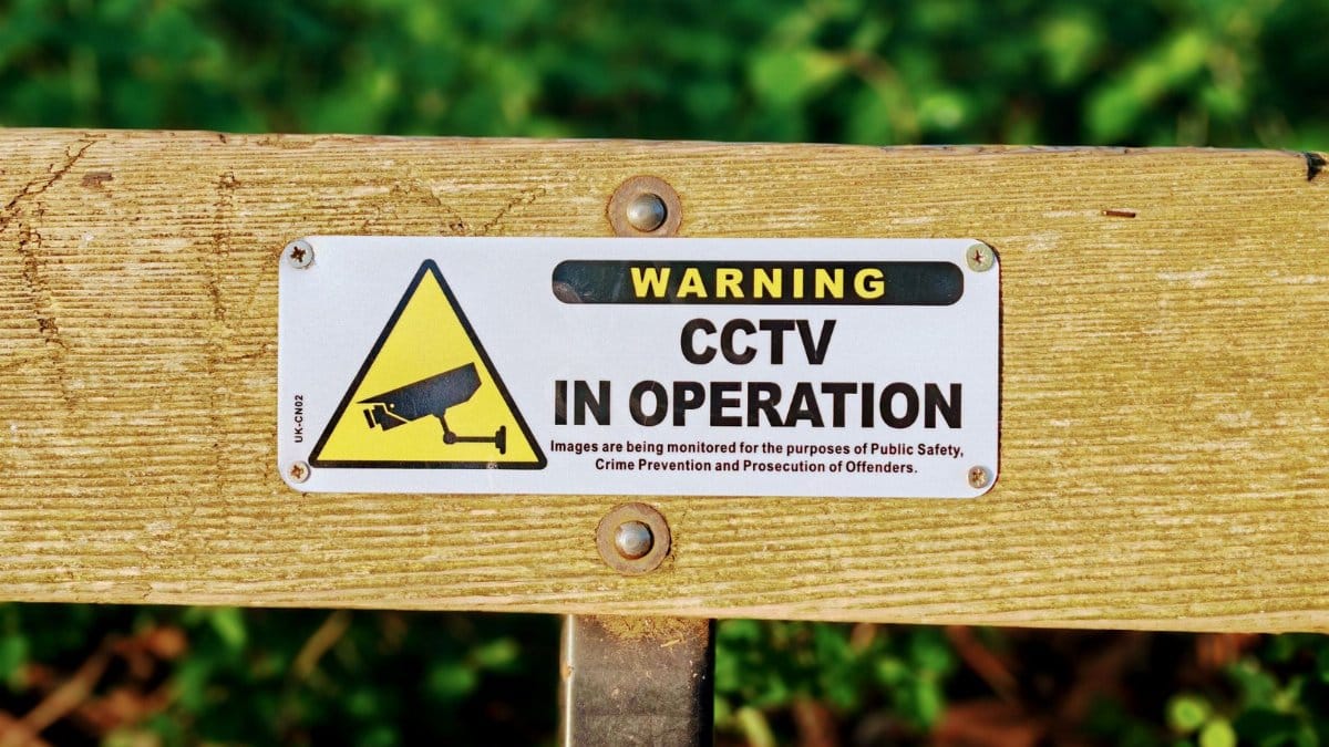 Wooden bench with a CCTV in operation warning sign, emphasizing public safety.