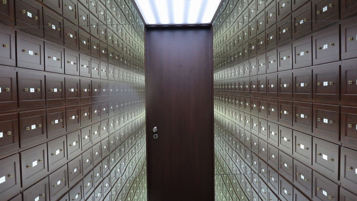 Wooden lockboxes line the walls of a modern, secure vault with a central wooden door.