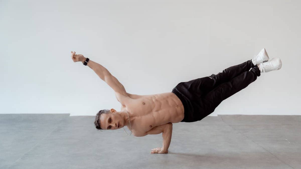 Athletic man in a one-handed handstand pose indoors, displaying strength and balance.
