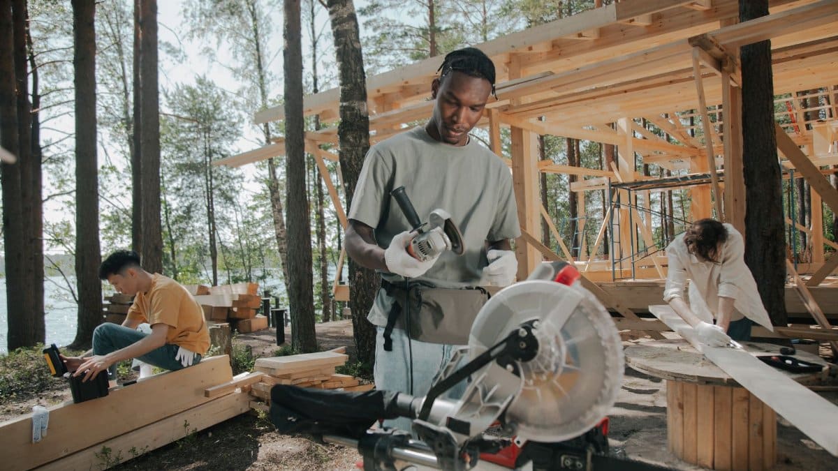 Construction crew building a wooden structure outdoors in a forest setting.
