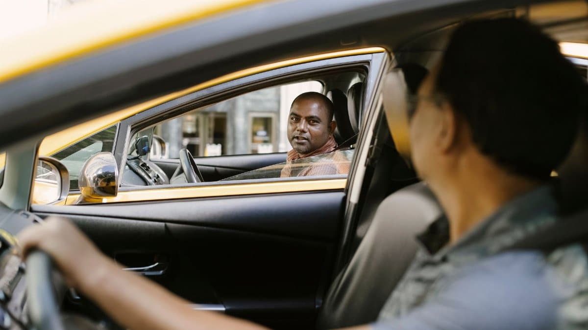 Side view of adult ethnic male cab driver interacting with anonymous colleague driving auto while looking at each other in city