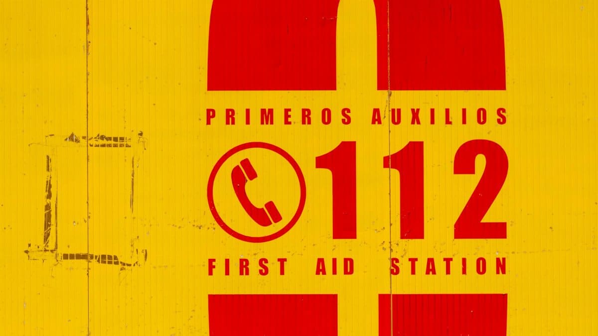 Bright yellow and red emergency sign indicating first aid station. Call 112 for emergencies.