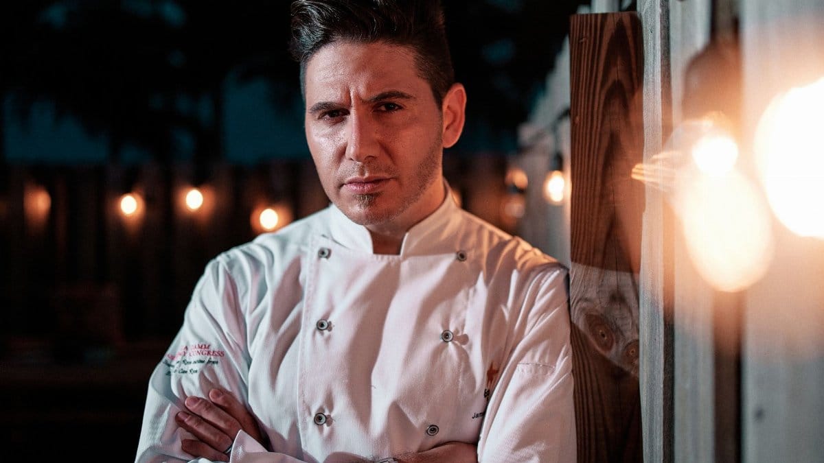 A confident chef poses with arms crossed at night in Miami, showcasing culinary expertise.