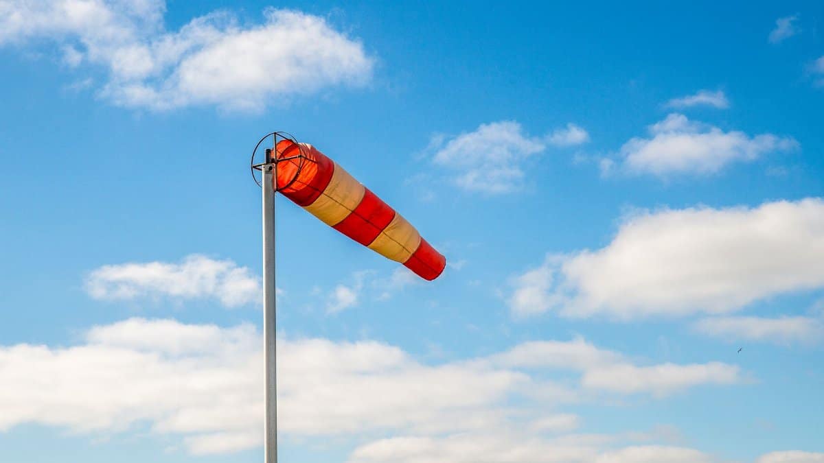 A vibrant windsock indicating wind direction against a picturesque blue sky with clouds.
