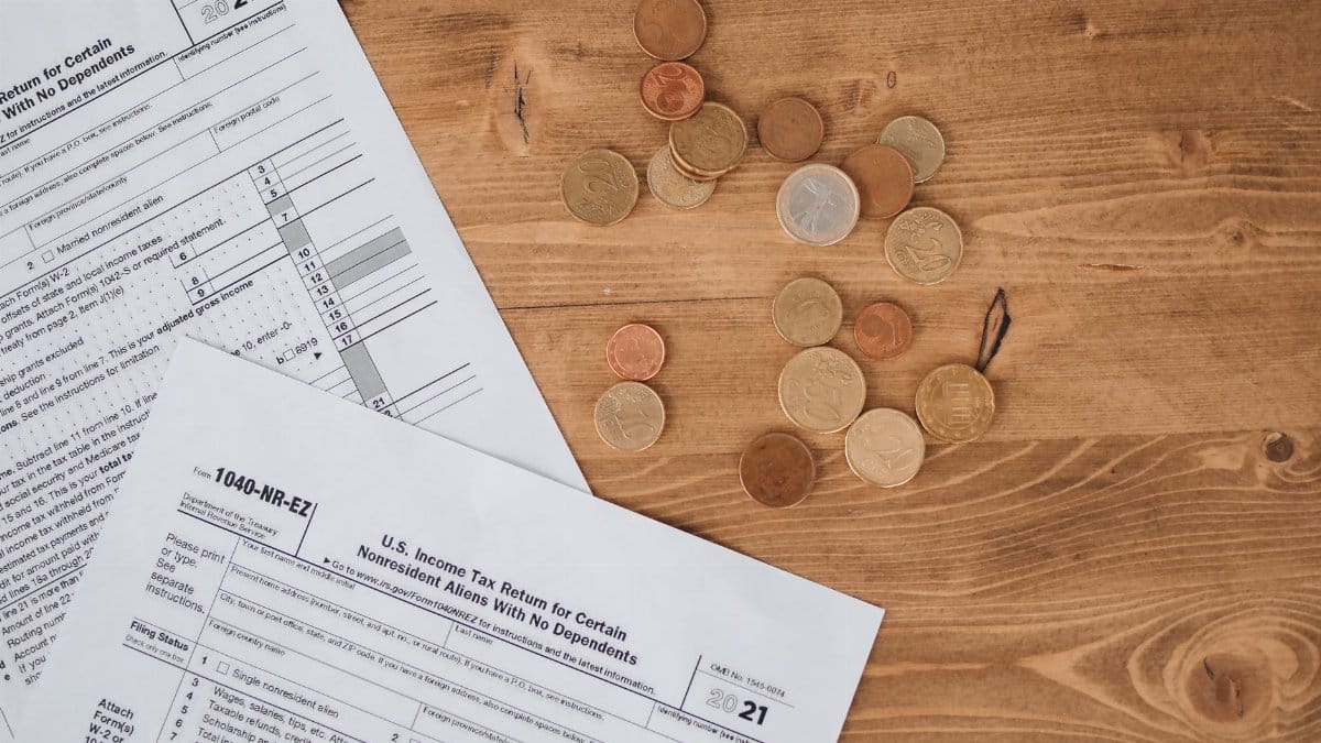 Flat lay of tax forms and scattered coins on a wooden table, illustrating finance and taxation concepts.