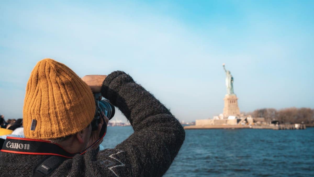 A person in a beanie capturing the Statue of Liberty across the water in New York City.