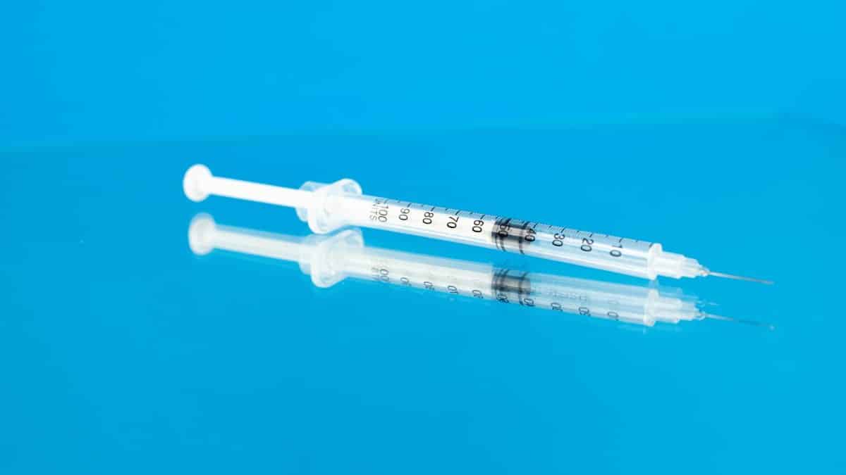 A syringe reflected on a glossy blue surface, symbolizing medicine and healthcare.