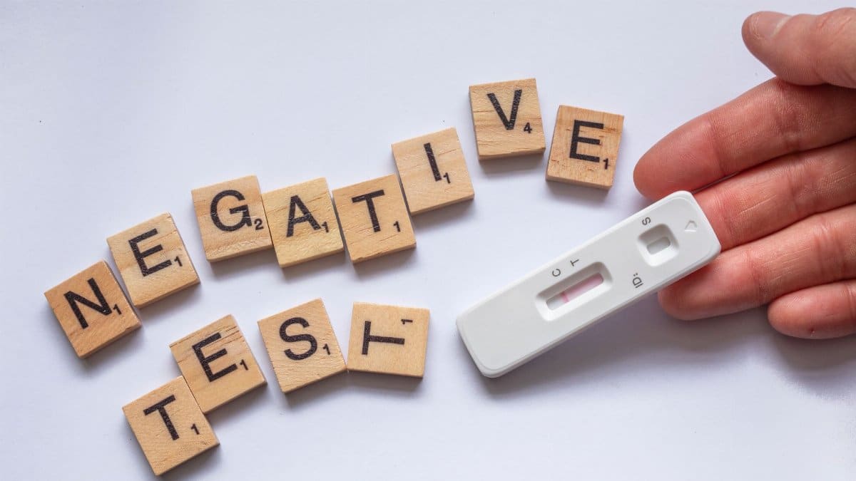 A negative test result displayed with scrabble letters and a test kit on a white surface.