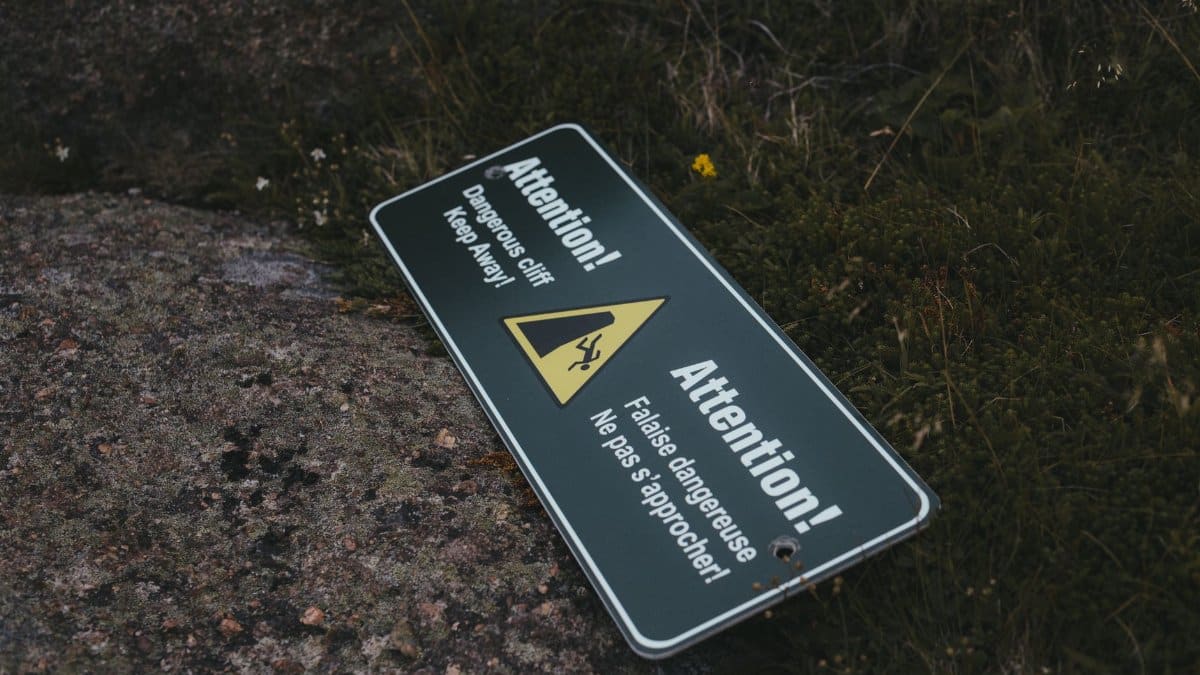 An outdoor warning sign saying 'Attention! Dangerous cliff. Keep away.' lying on rocky ground.