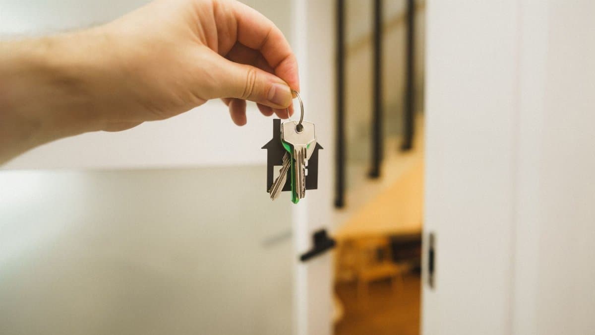 A hand holding a house key indoors signifies new ownership or leasing in real estate.