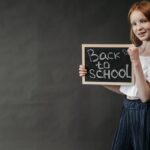 Young girl holding a 'Back to School' chalkboard, ready for the school year.