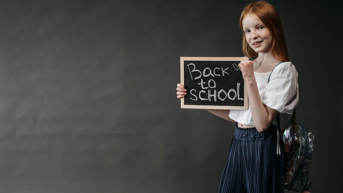 Young girl holding a 'Back to School' chalkboard, ready for the school year.