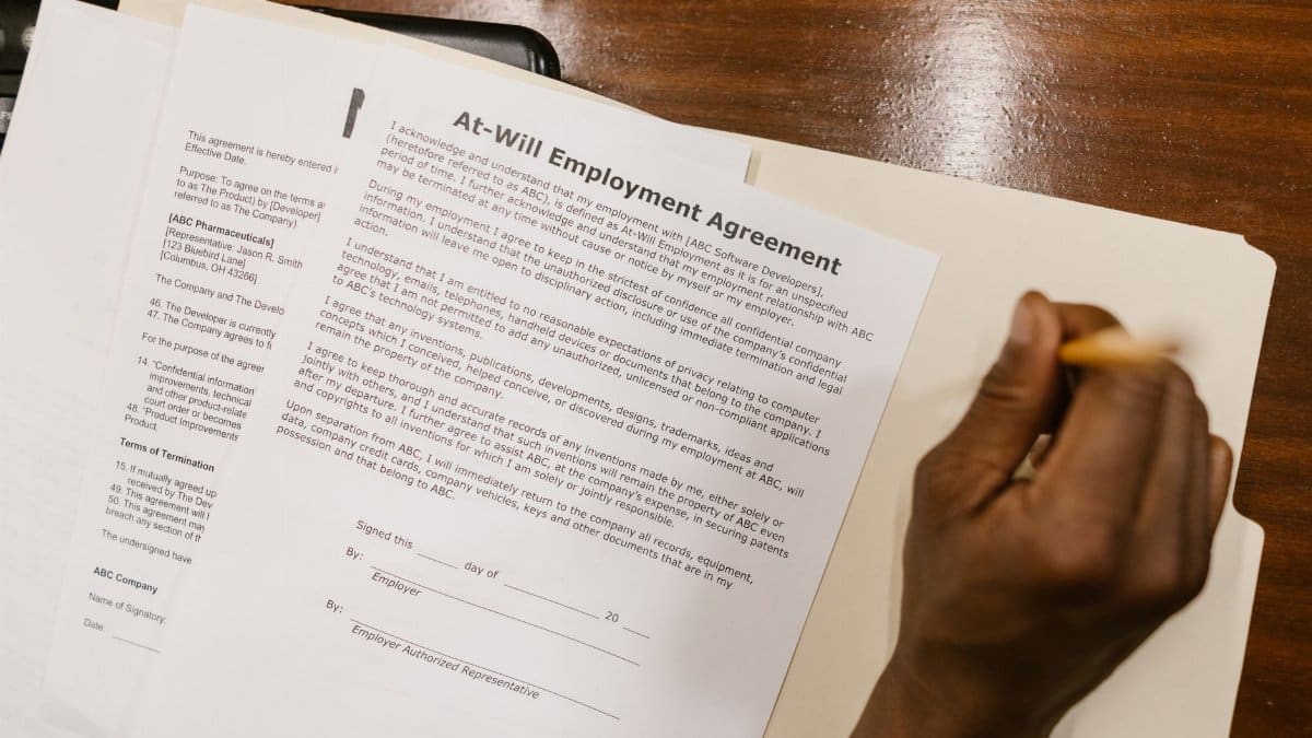 Close-up of a hand signing an at-will employment agreement on a wooden desk.