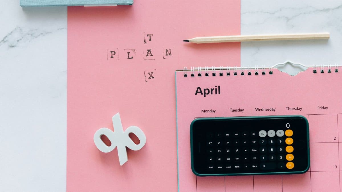 Flat lay of April calendar with calculator, pencil, and pink background for financial planning.