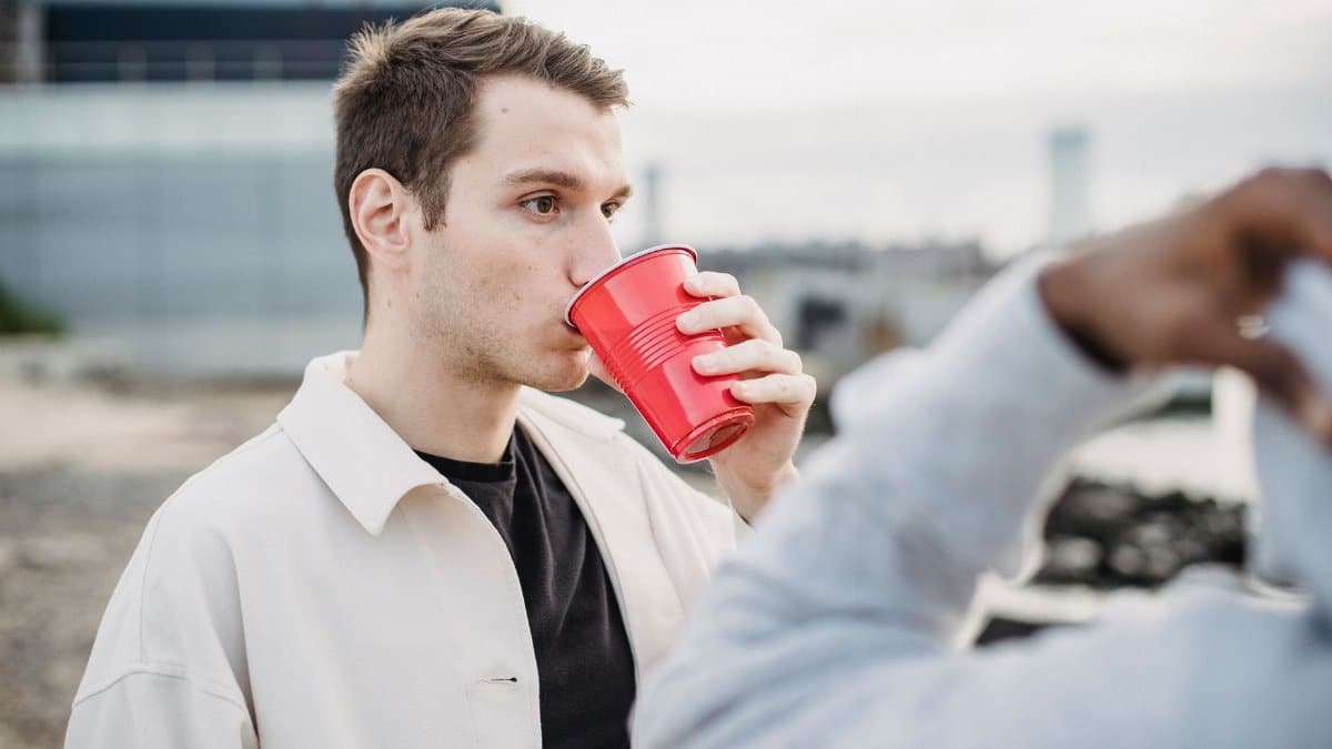 Male drinking beverage from disposable red cup standing with African American friend on street