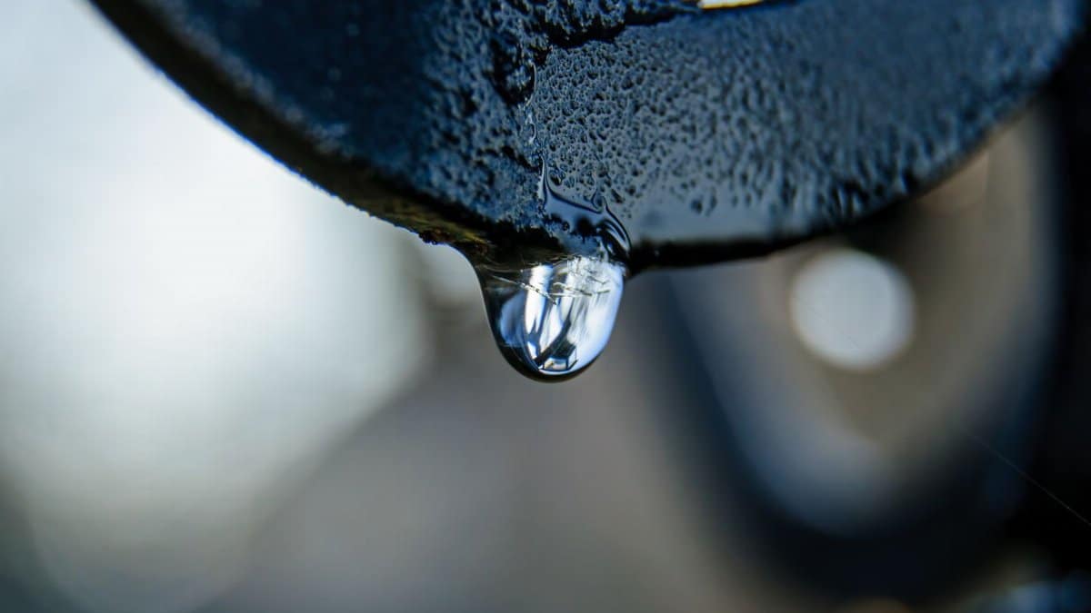 Macro shot of a dew drop hanging from a metal surface, reflecting light.