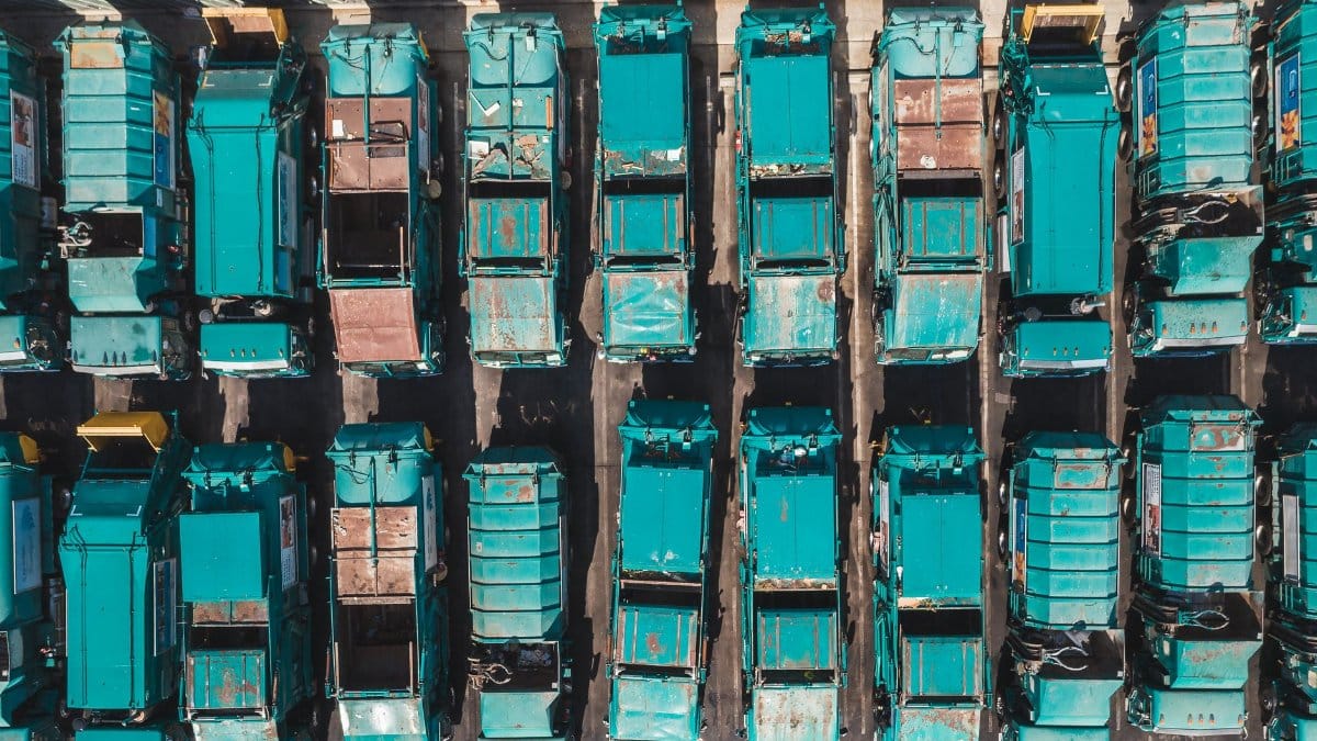Aerial shot of turquoise garbage trucks parked in neat rows, showcasing a pattern of urban utility vehicles.