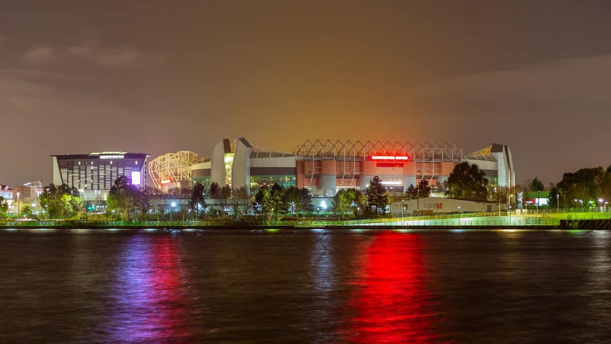 A stunning view of Old Trafford Stadium reflected in water at night in Manchester, UK.