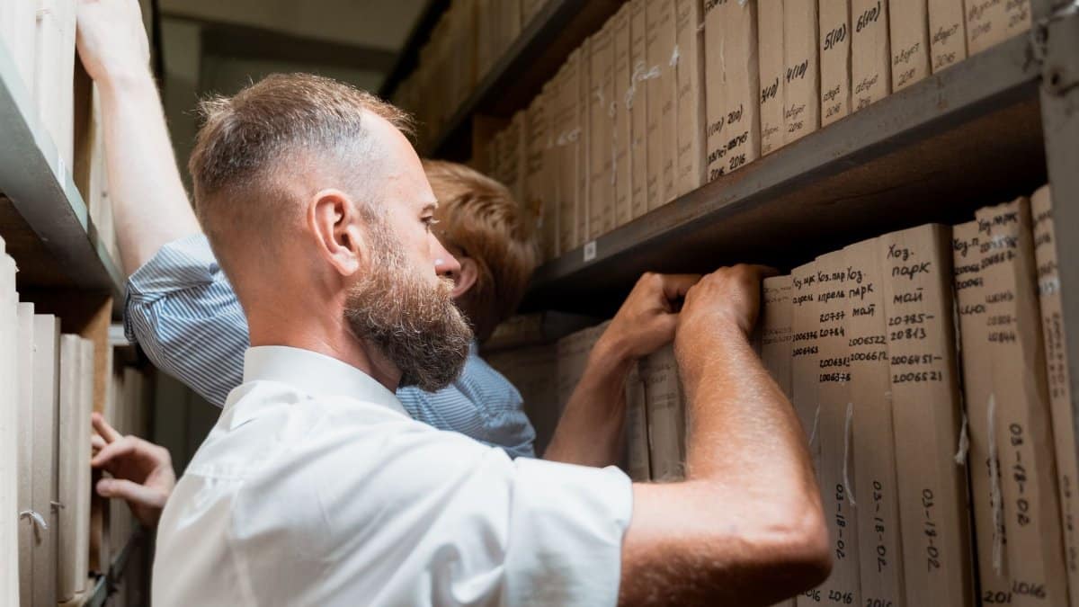 Two men organizing paperwork in an archive, focused on meticulous documentation.