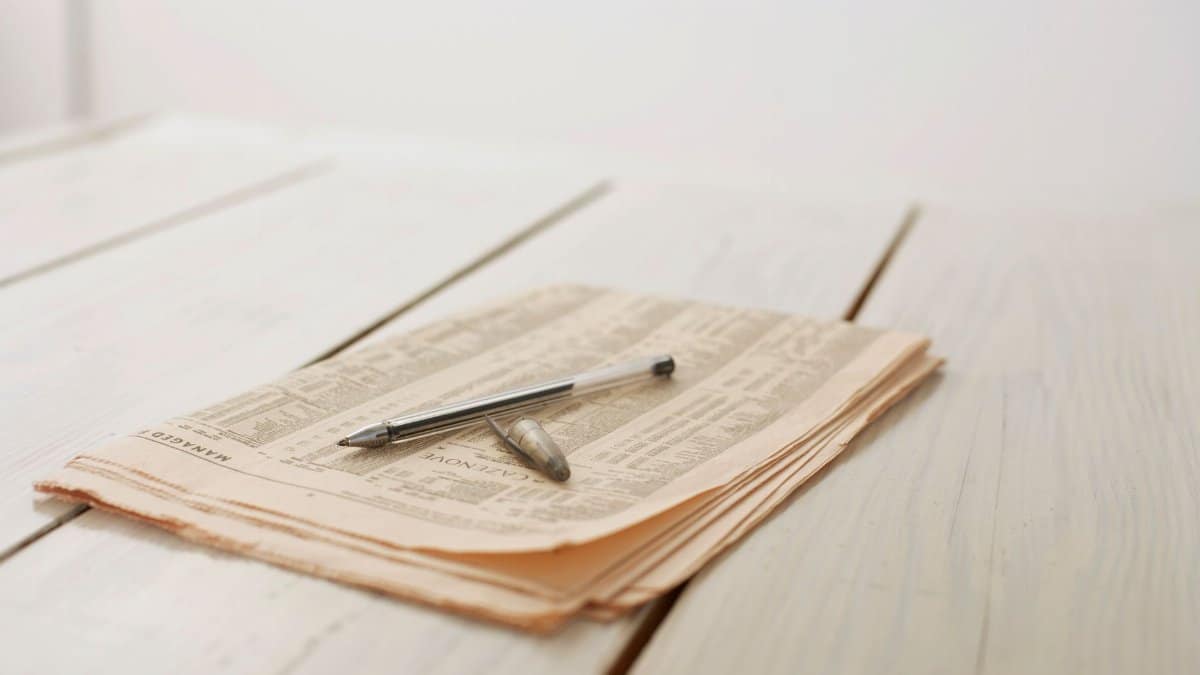 Elegant close-up of a newspaper with a pen on a wooden table, highlighting simplicity and calm.