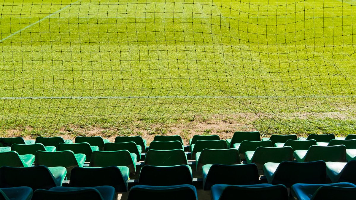 A view from empty stadium seats overlooking a sunny soccer field during the day.