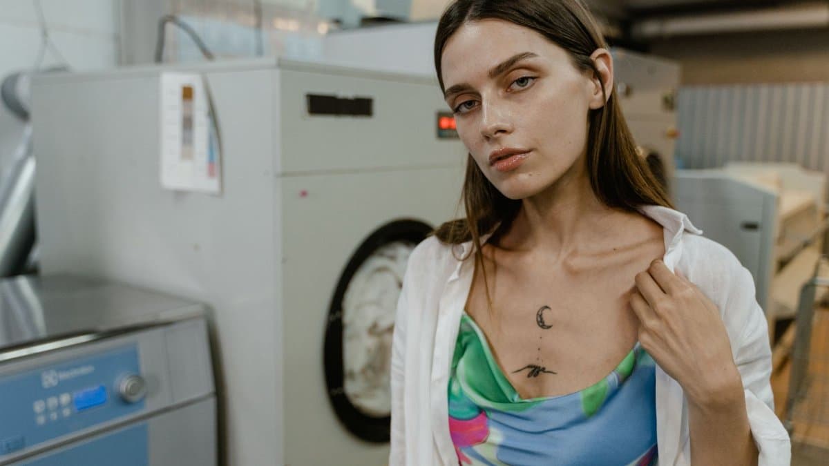 Stylish woman posing in front of industrial washing machines in a laundromat.