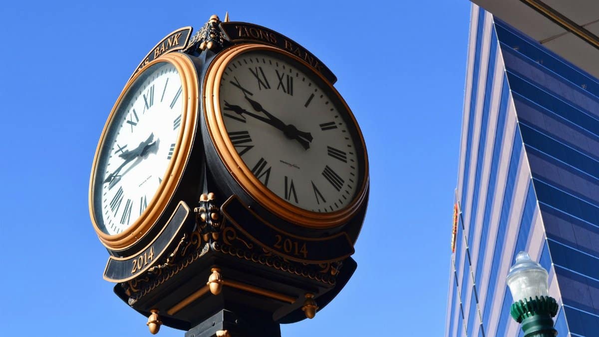 Elegant urban clock tower with Roman numerals against a clear blue sky and modern architecture.