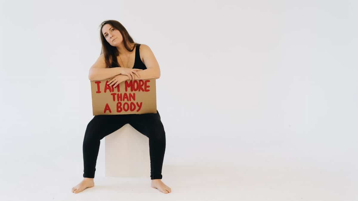 Woman holding 'I am more than a body' sign, promoting empowerment and equality.
