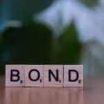 Scrabble tiles spelling 'Bond' on a wooden table with a blurred green background.