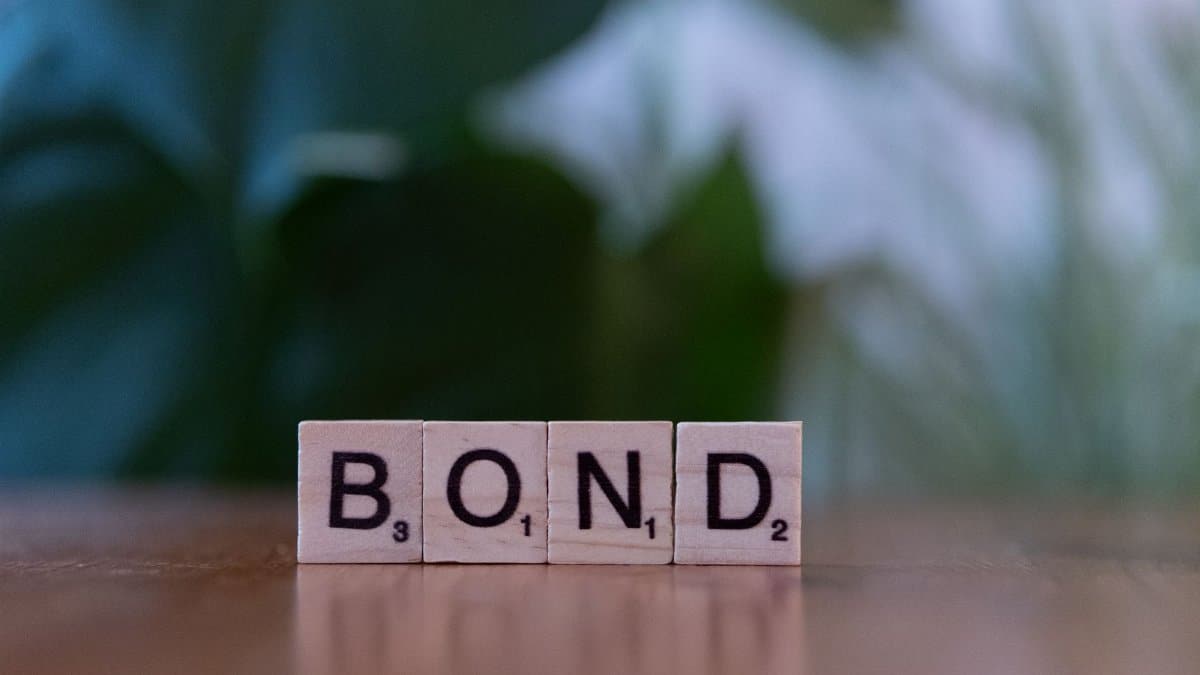 Scrabble tiles spelling 'Bond' on a wooden table with a blurred green background.