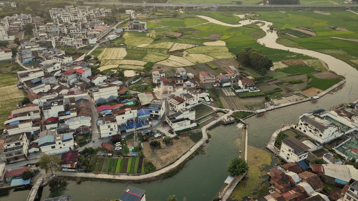 Aerial shot of a rural village surrounded by sprawling farmland and a river bend.