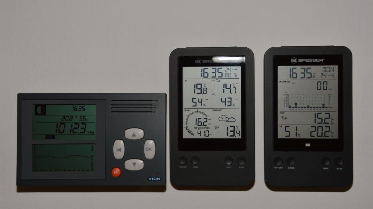 Multiple digital weather monitors on a wall displaying temperature and pressure.