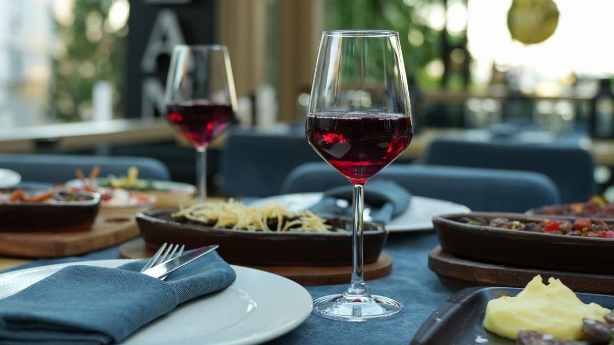 Close-up of a glass of red wine on a table set with gourmet dishes in a stylish restaurant setting.