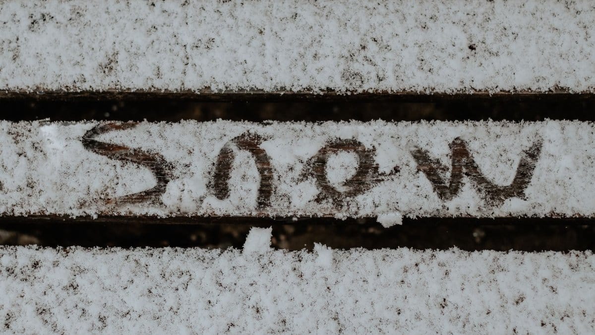 Snow covered wooden slats with 'snow' written in them, conveying winter chill.