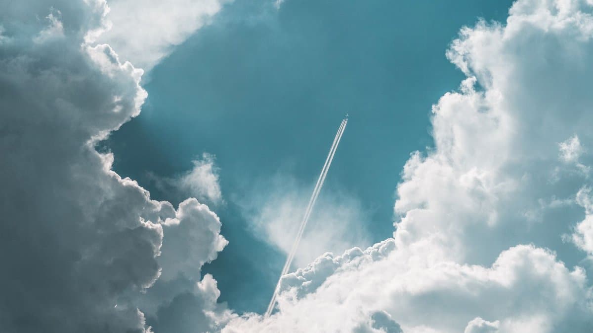 An airplane soars high above Ilmenau, Germany, leaving a trail amidst dramatic clouds.