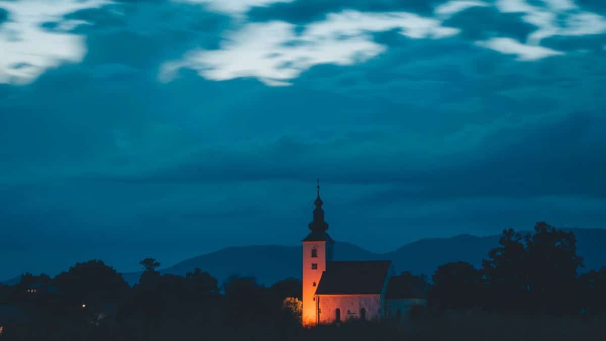 Tranquil scene of a countryside church illuminated at twilight against a cloudy sky.