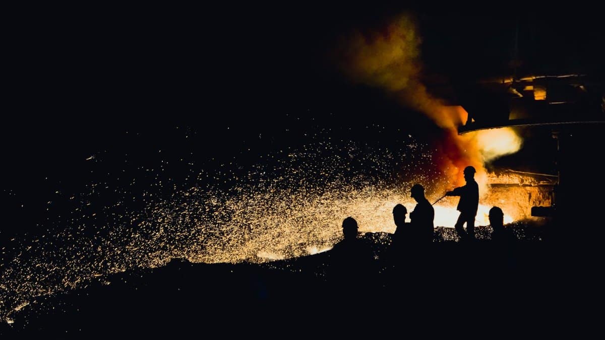 Dramatic image of foundry workers silhouetted against fiery sparks and molten metal.