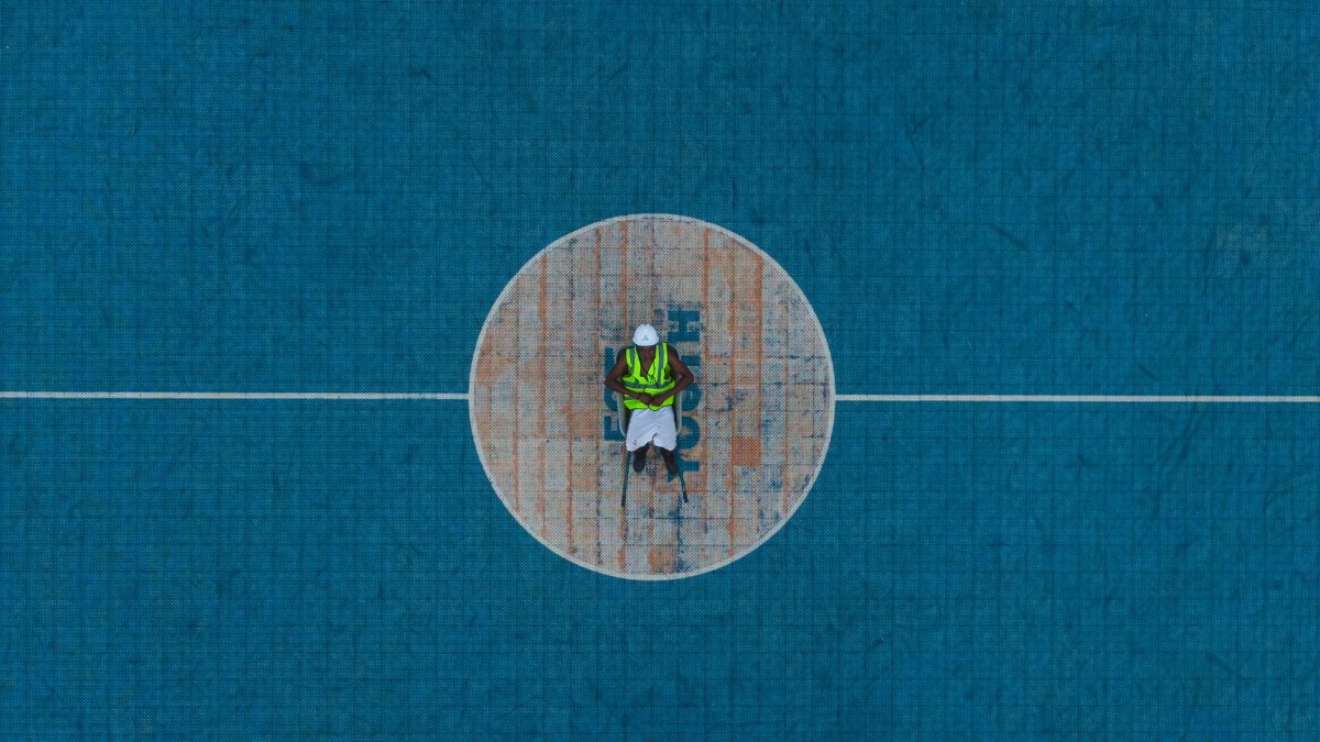 Aerial shot of a worker in safety gear standing at the center of a basketball court.
