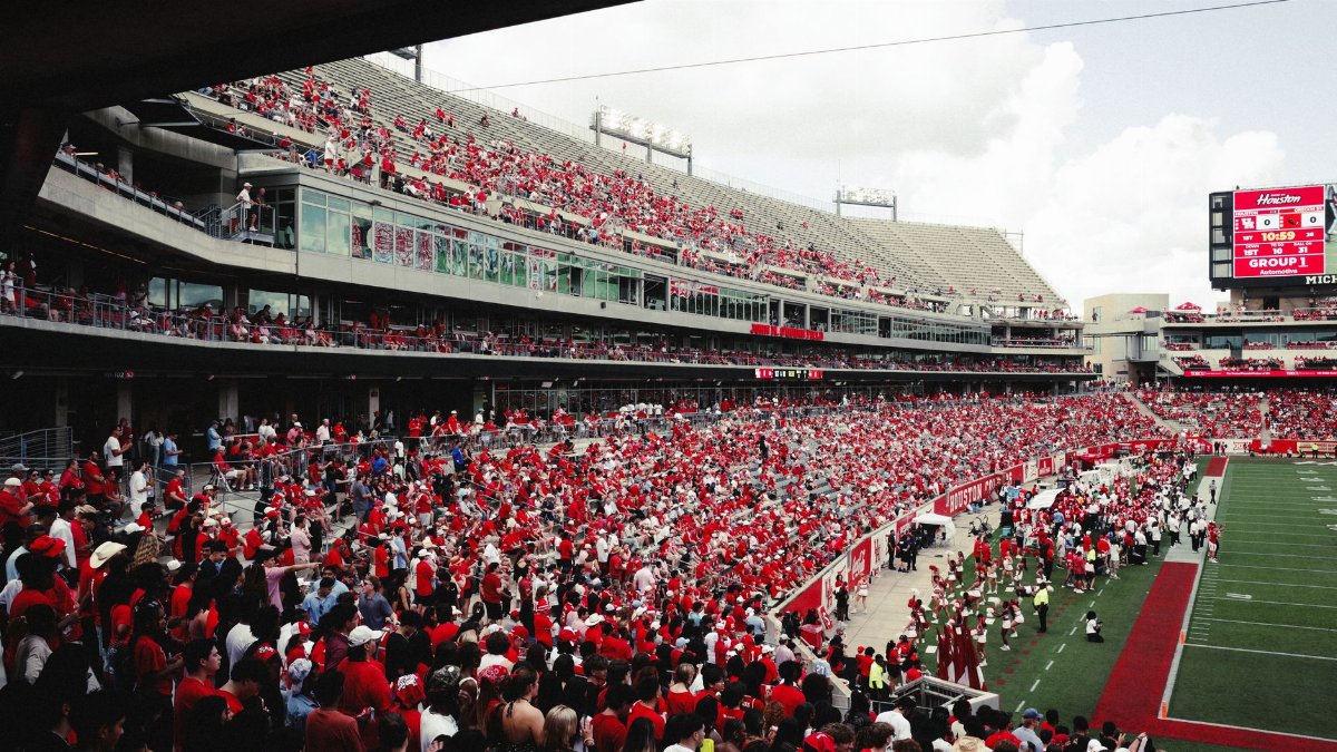 A vibrant crowd in a stadium cheering during an outdoor football game, creating an energetic atmosphere.