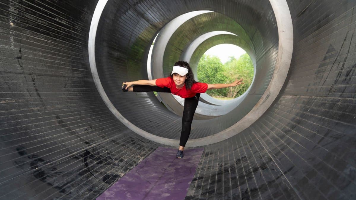 Woman in a red top doing yoga pose inside a futuristic tunnel, promoting health and wellness.
