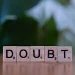 Close-up of Scrabble tiles spelling 'doubt' on a wooden surface, conveying uncertainty.