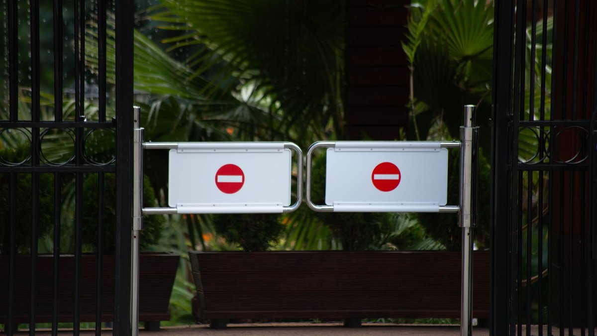 Metal gates with no entry signs at a lush garden entrance, conveying restricted access.