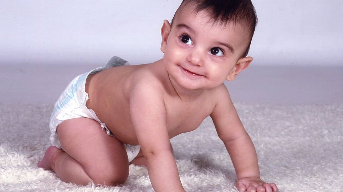 Cute baby boy in diaper crawling and smiling indoors on a fluffy carpet.