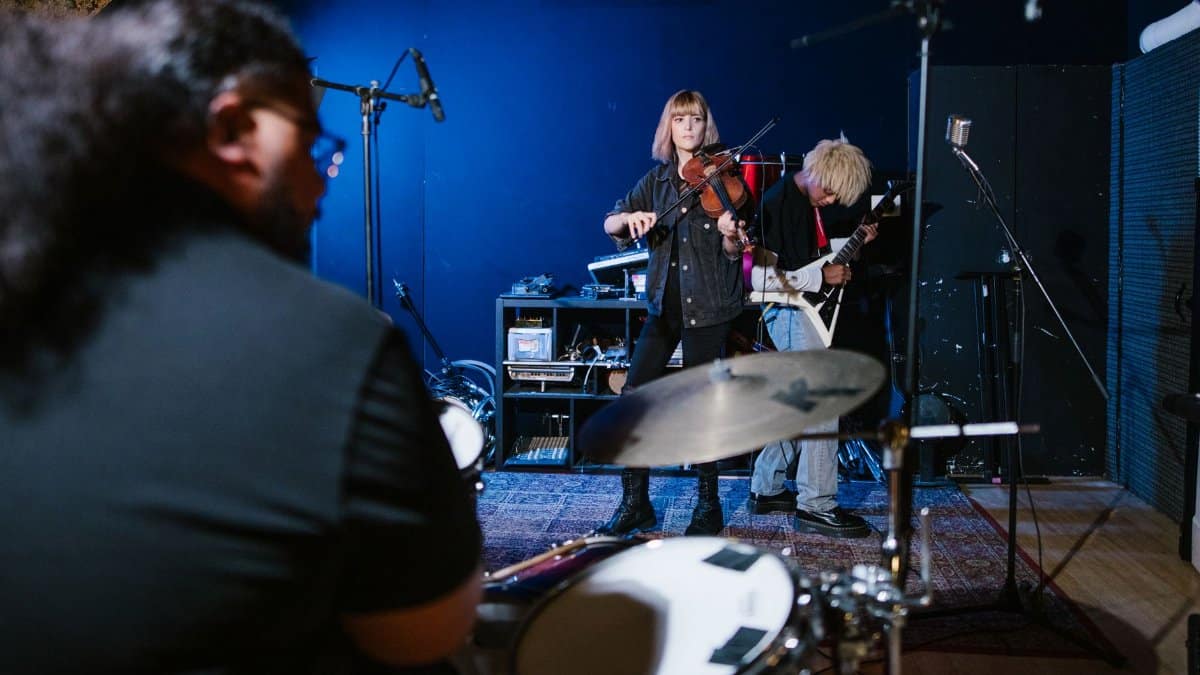 Band rehearsal with violin, guitar, and drums in an indoor studio.