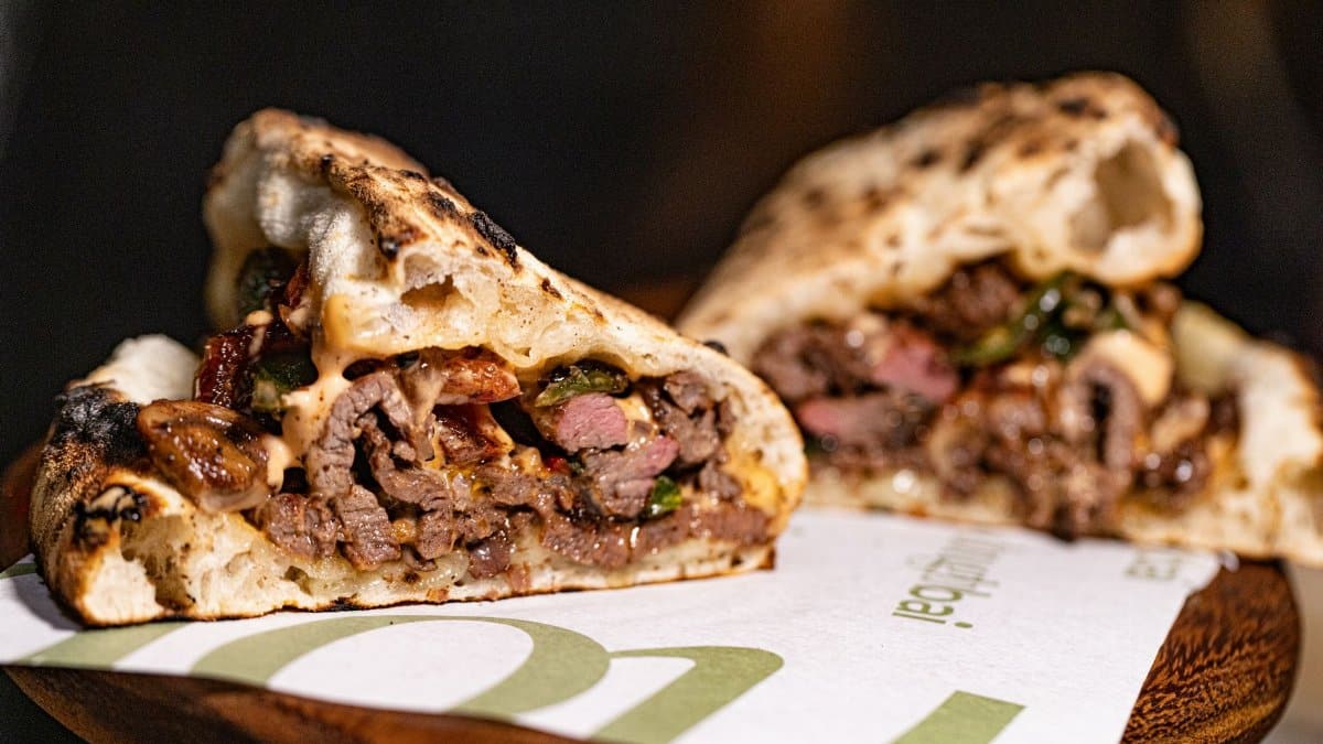 Gourmet grilled meat sandwich with melted cheese and vegetables.