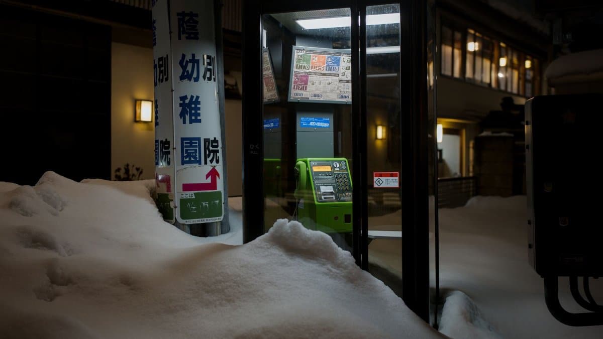 A snowy phone booth at night in Kanazawa, Ishikawa, Japan featuring a green payphone.