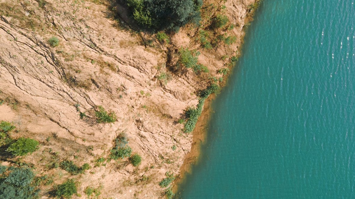 A stunning aerial shot depicting a rugged cliffside meeting a serene body of water.