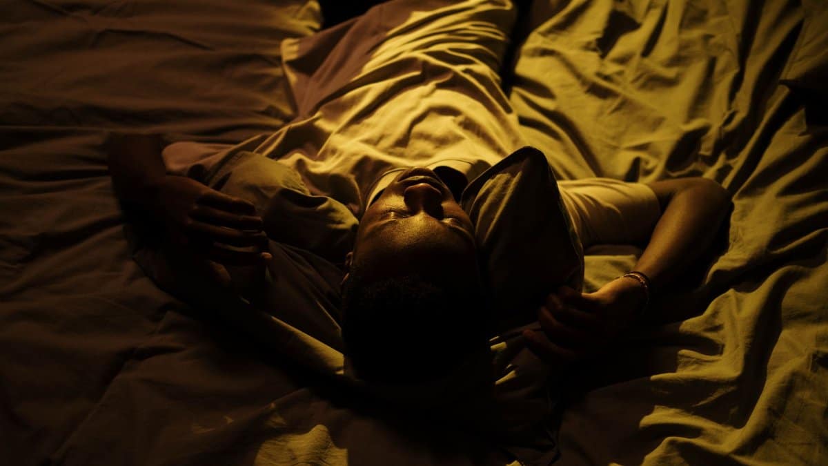 A man lies in bed at night, struggling with insomnia in a dimly lit room.