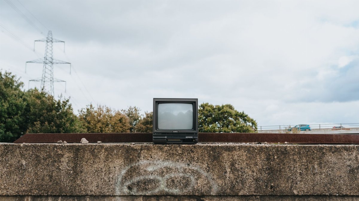 Obsolete retro black television placed on shabby concrete barrier with graffiti against cloudy sky in city on street with trees
