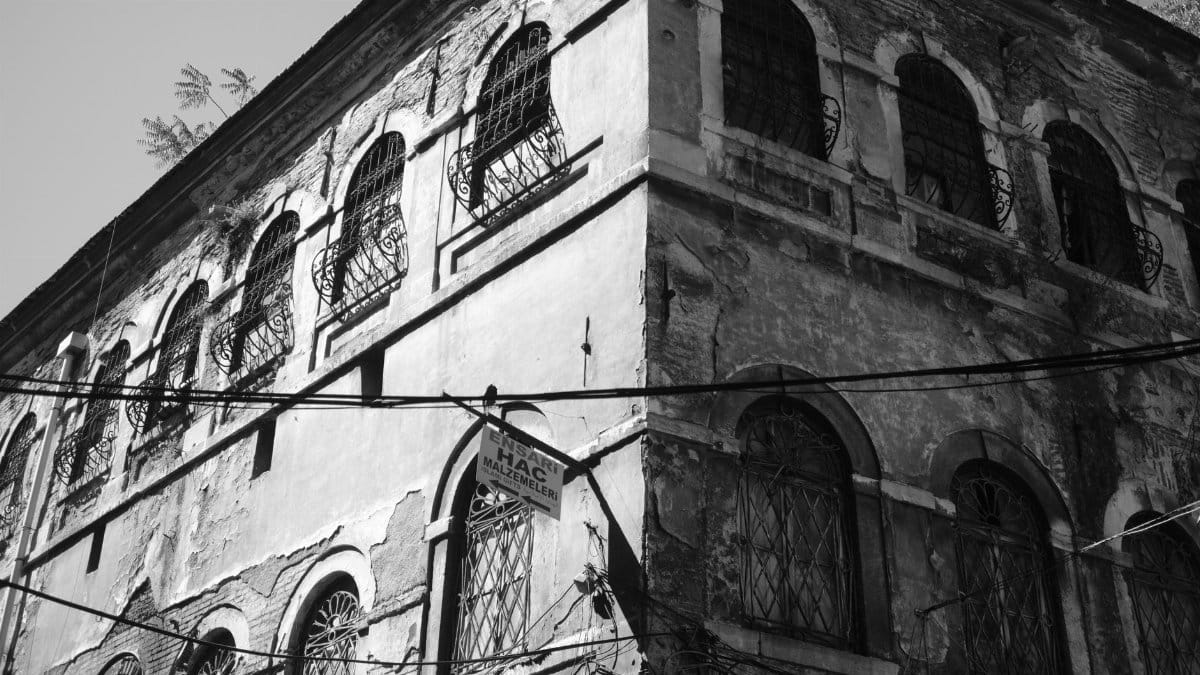 Black and white photo of an old weathered building with arched windows in urban setting.